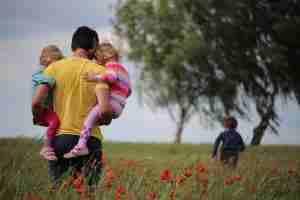 Parent carrying two children on hips walking through a field of flowers