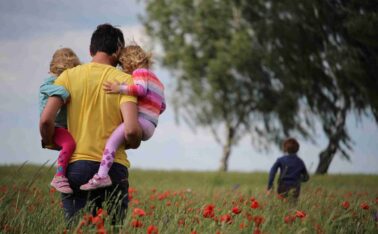 Parent carrying two children on hips walking through a field of flowers