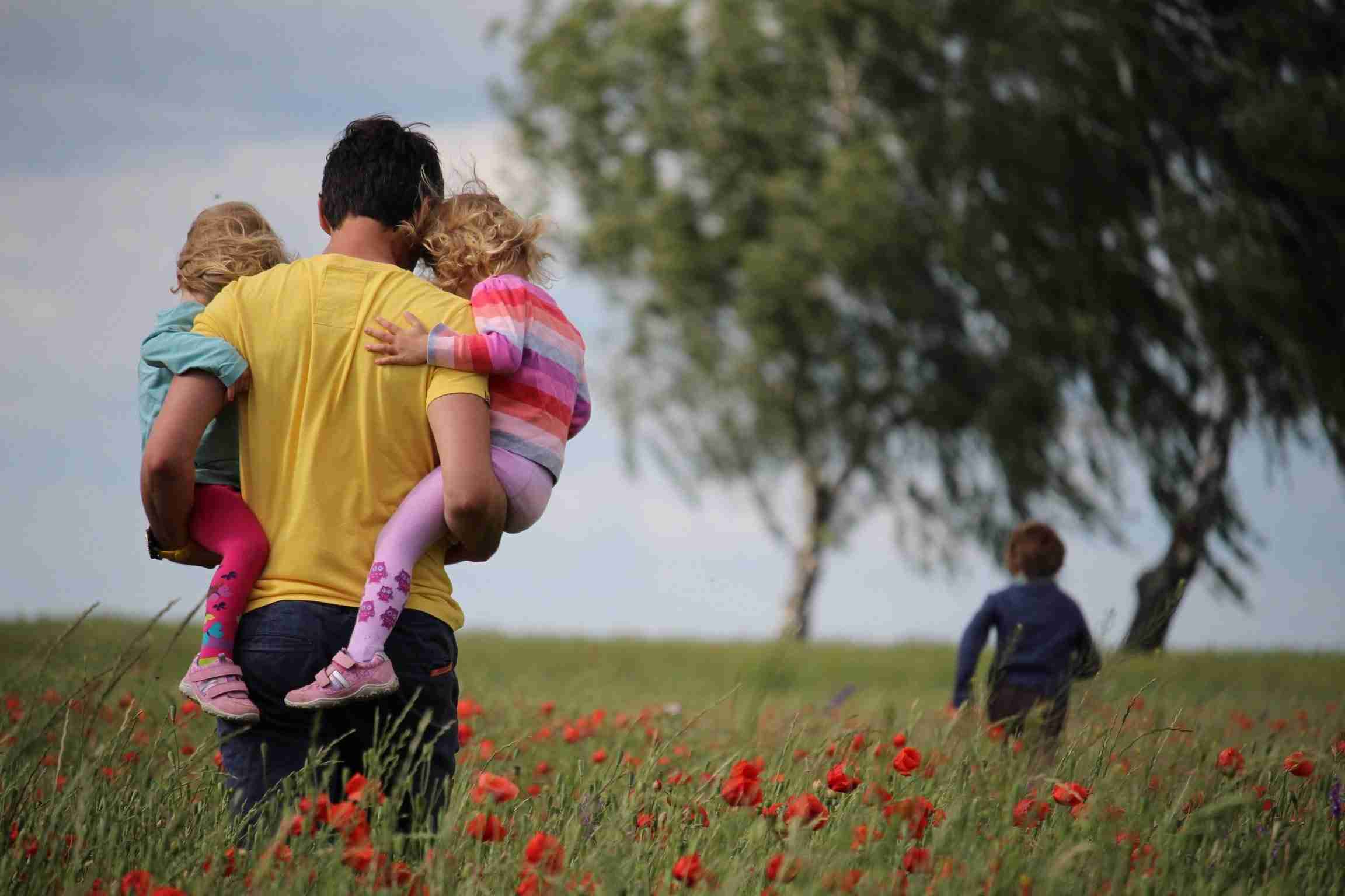 Parent carrying two children on hips walking through a field of flowers