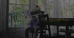 Elderly male sitting down reading newspaper