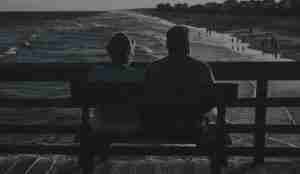 Elderly couple sitting on pier looking out towards beach