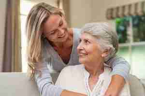 Daughter hugging her elderly mother from behind on couch