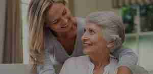Daughter hugging her elderly mother from behind on couch