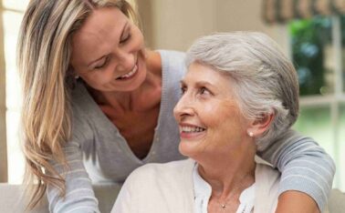 Daughter hugging her elderly mother from behind on couch