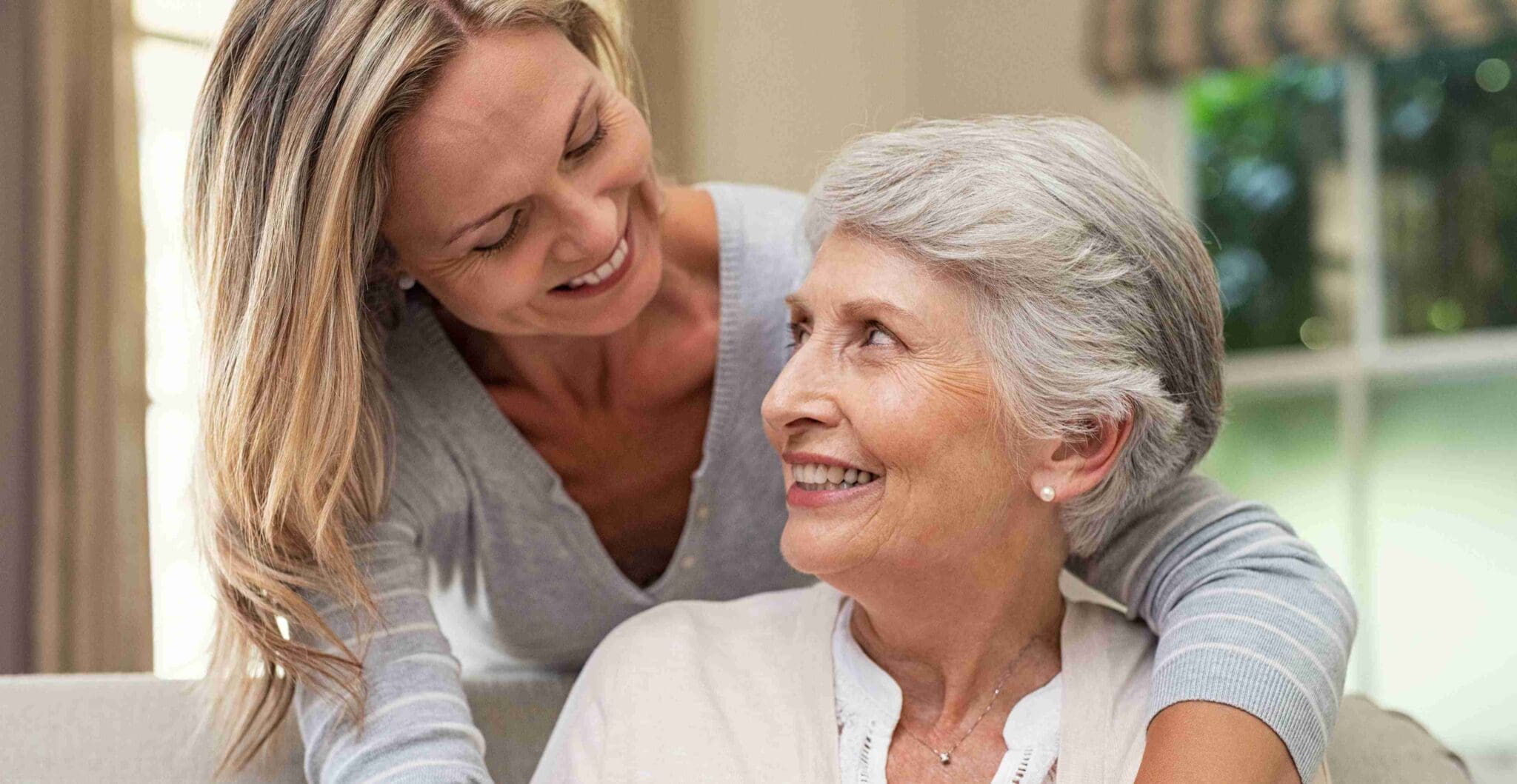 Daughter hugging her elderly mother from behind on couch