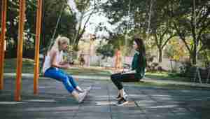 Two teenage girls facing each other on a swingset