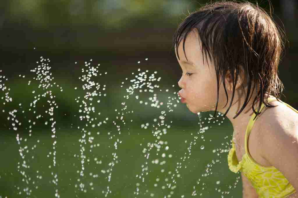 Toddler drinking from the water fountain in the summertime.