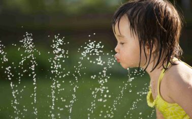 Toddler drinking from the water fountain in the summertime.