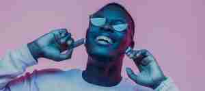 Young african man listening to music with earphones, dancing isolated on pink background
