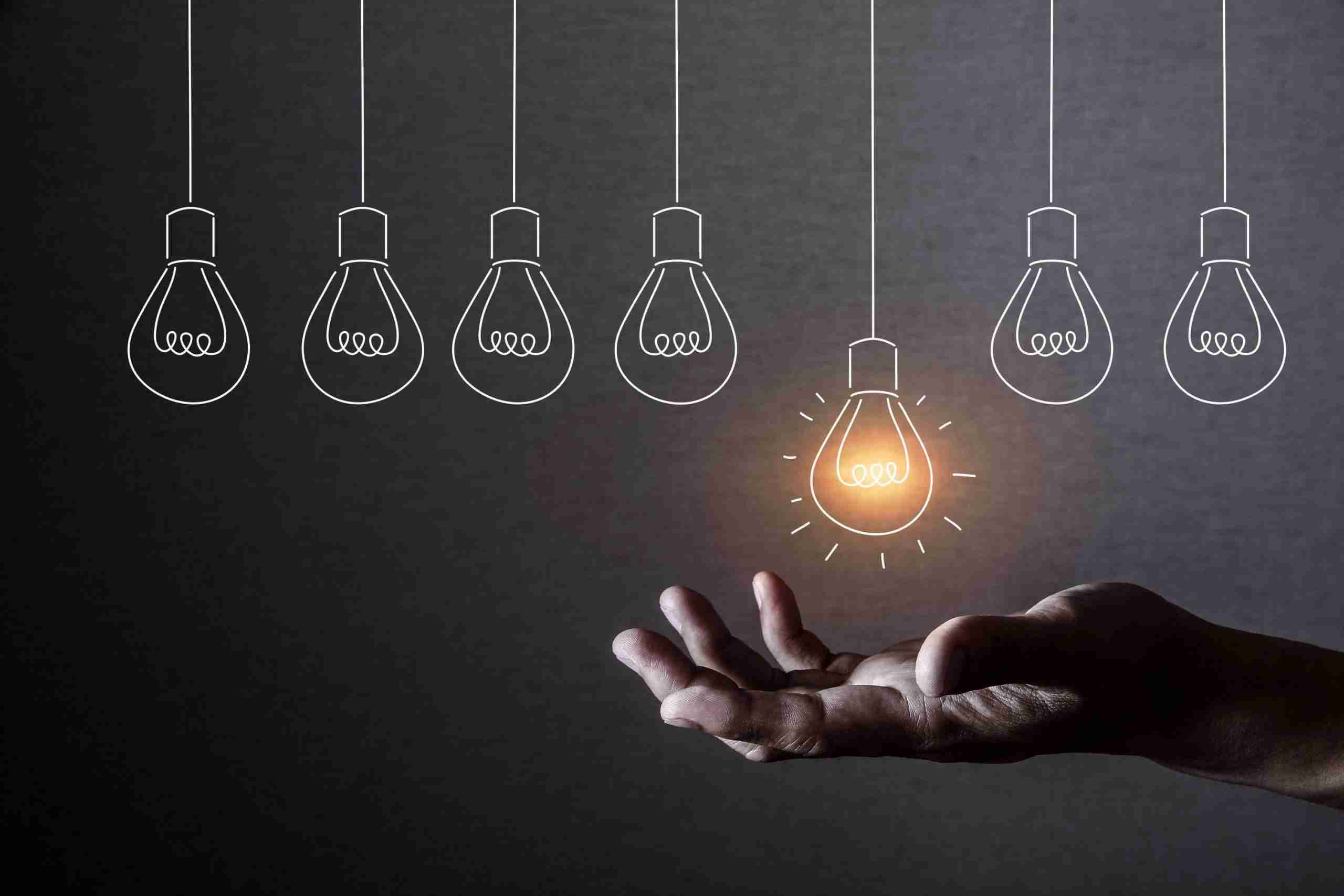 A picture of a set of hanging lightbulbs, with a hand situated underneath to grab them. This signifies the importance of capturing the insights and ideas of staff and customers in crafting an effective innovation strategy.